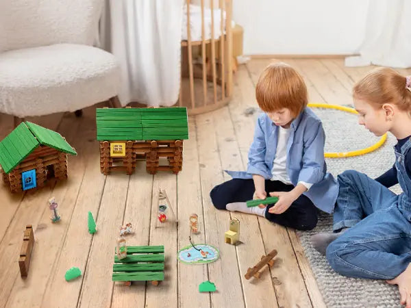 Two children playing with toy houses and figures on a wooden floor.