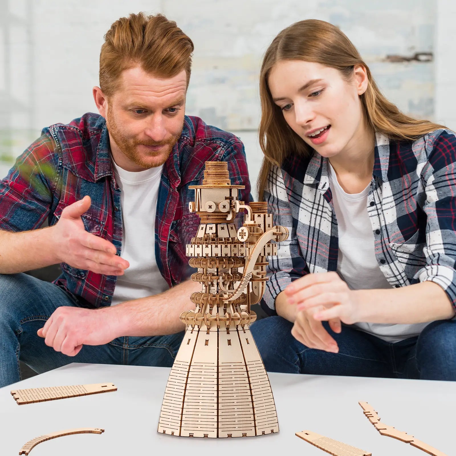 Two people examining a wooden mechanical model on a table.