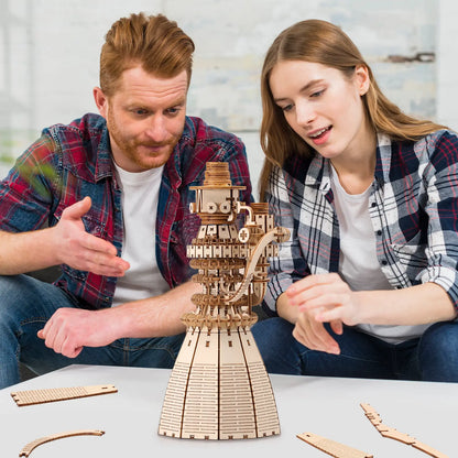 Two people examining a wooden mechanical model on a table.