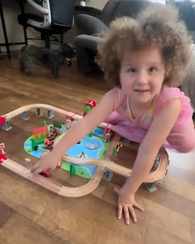 Child playing with a wooden train set on a wooden floor.
