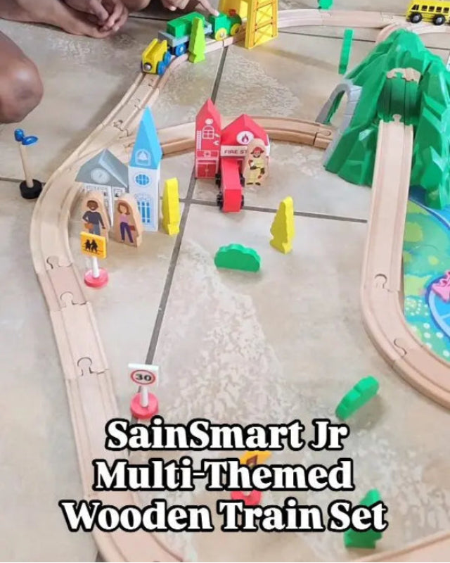 Colorful wooden train set with tracks and buildings on a table, featuring SainSmart Jr branding.