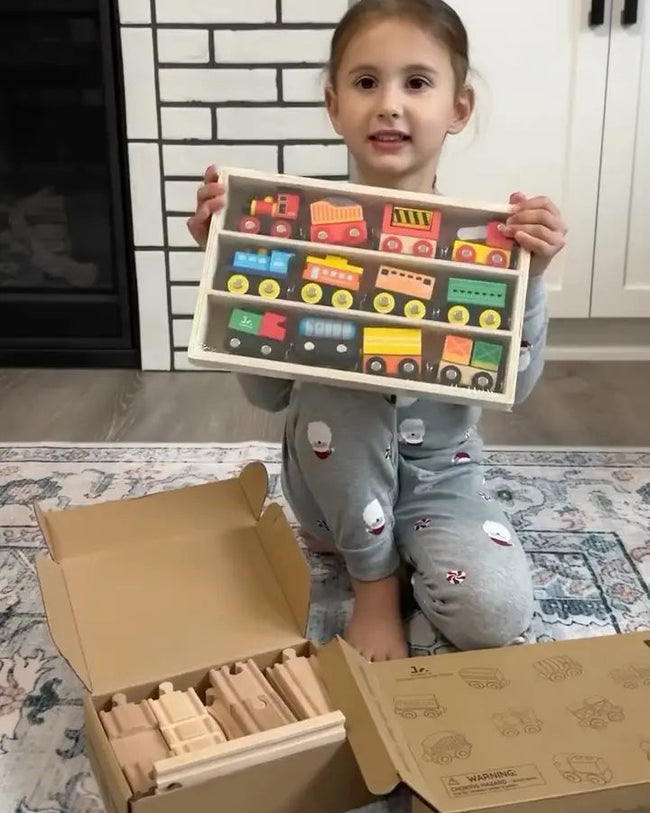 Child holding a toy train set in a living room with a fireplace and white brick wall.