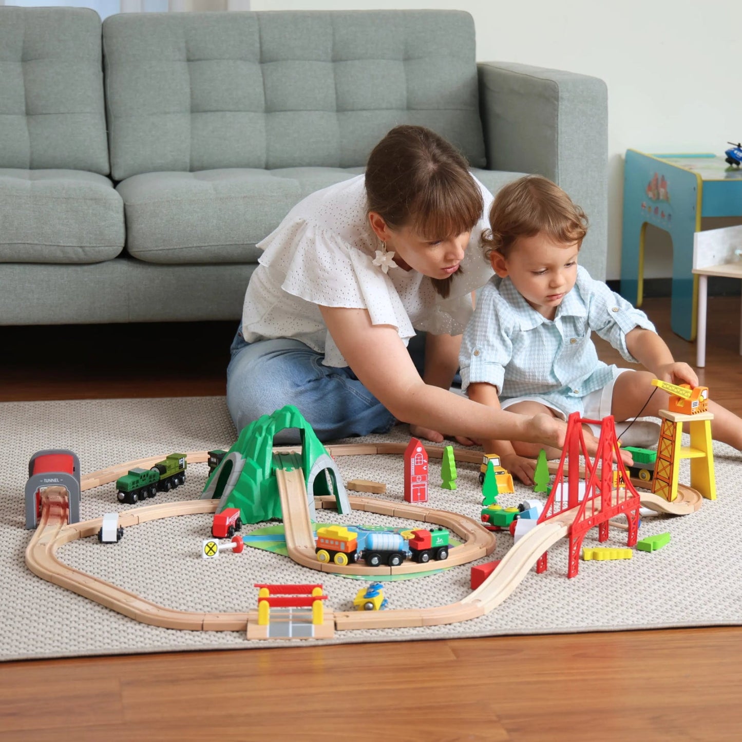 Two children playing with a toy train set on the floor in a living room.