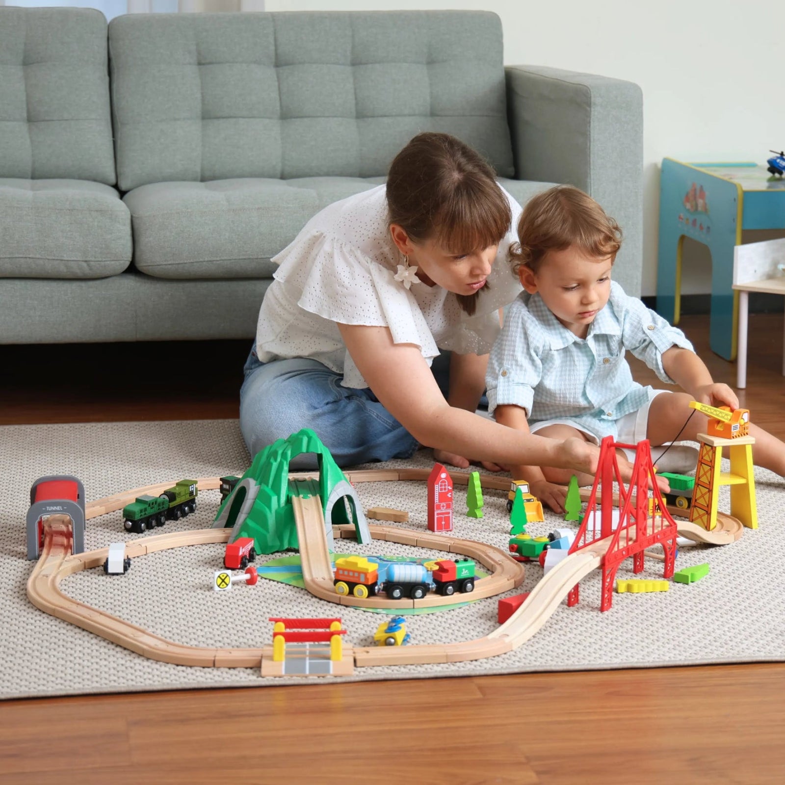 Two children playing with a toy train set on the floor in a living room.