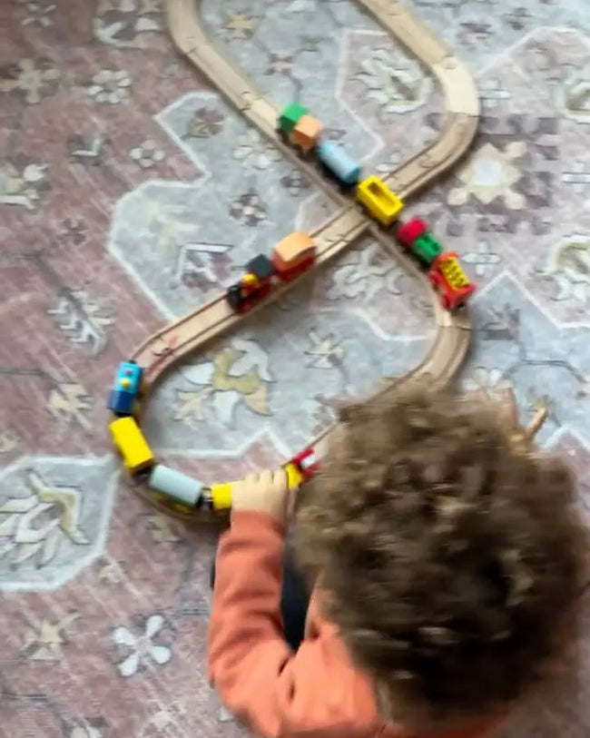 Child playing with a toy train set on a patterned rug