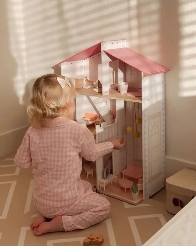 Child playing with a dollhouse in a room with sunlight filtering through curtains.