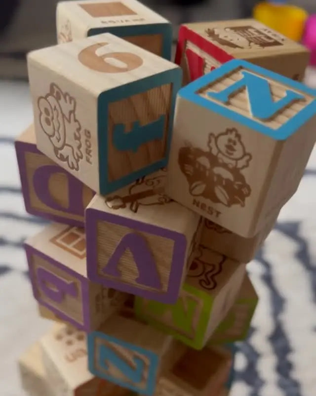 Stack of colorful wooden blocks with letters and symbols on a patterned surface