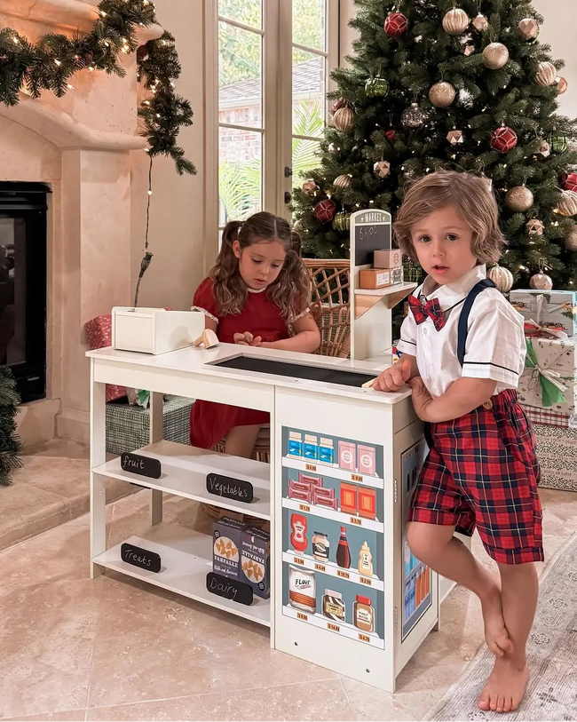 Children playing with a toy kitchen set in a room decorated for Christmas.