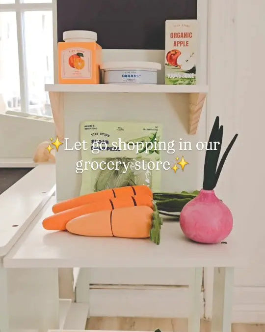 Toy grocery store setup with a chalkboard, fruits, and vegetables on a white surface.