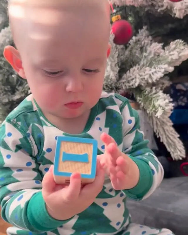 Child holding a wooden block with the number one in front of a Christmas tree.