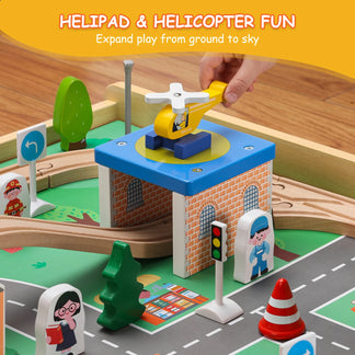 Toy helicopter on a helipad with a hand placing it, surrounded by a toy town setup.