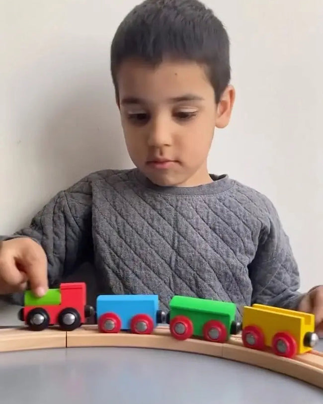 Child playing with a colorful wooden toy train set on a plain background