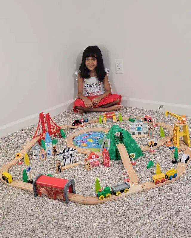 Child playing with a large wooden toy train set on the floor.