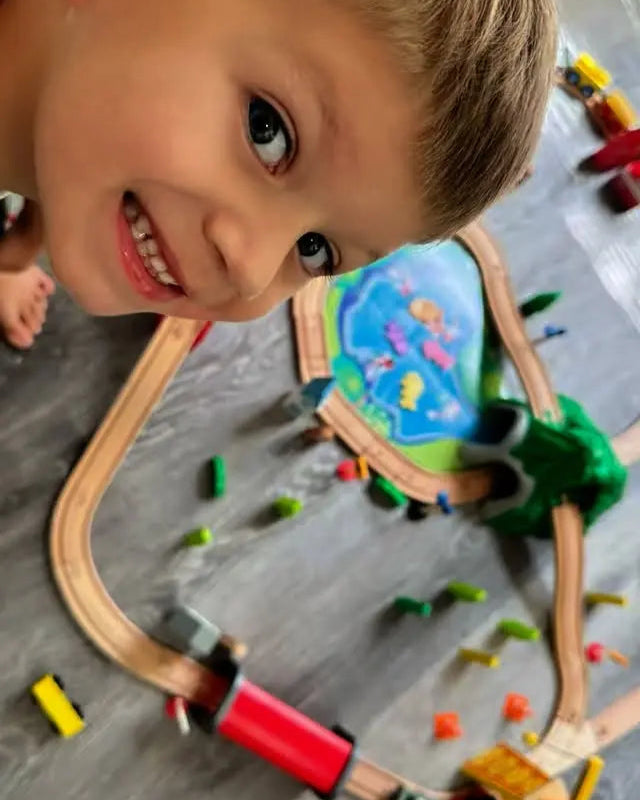 Child playing with a toy train set on a wooden floor