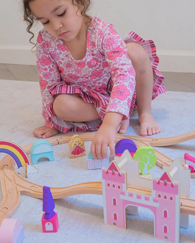 Child playing with toy castle and train set on a light-colored floor.