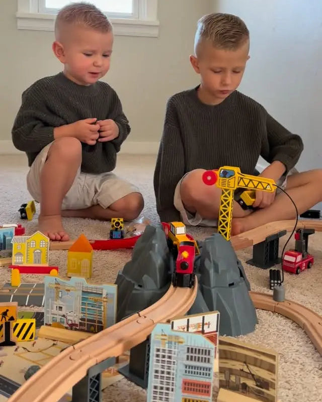 Two children playing with a toy train set on the floor.