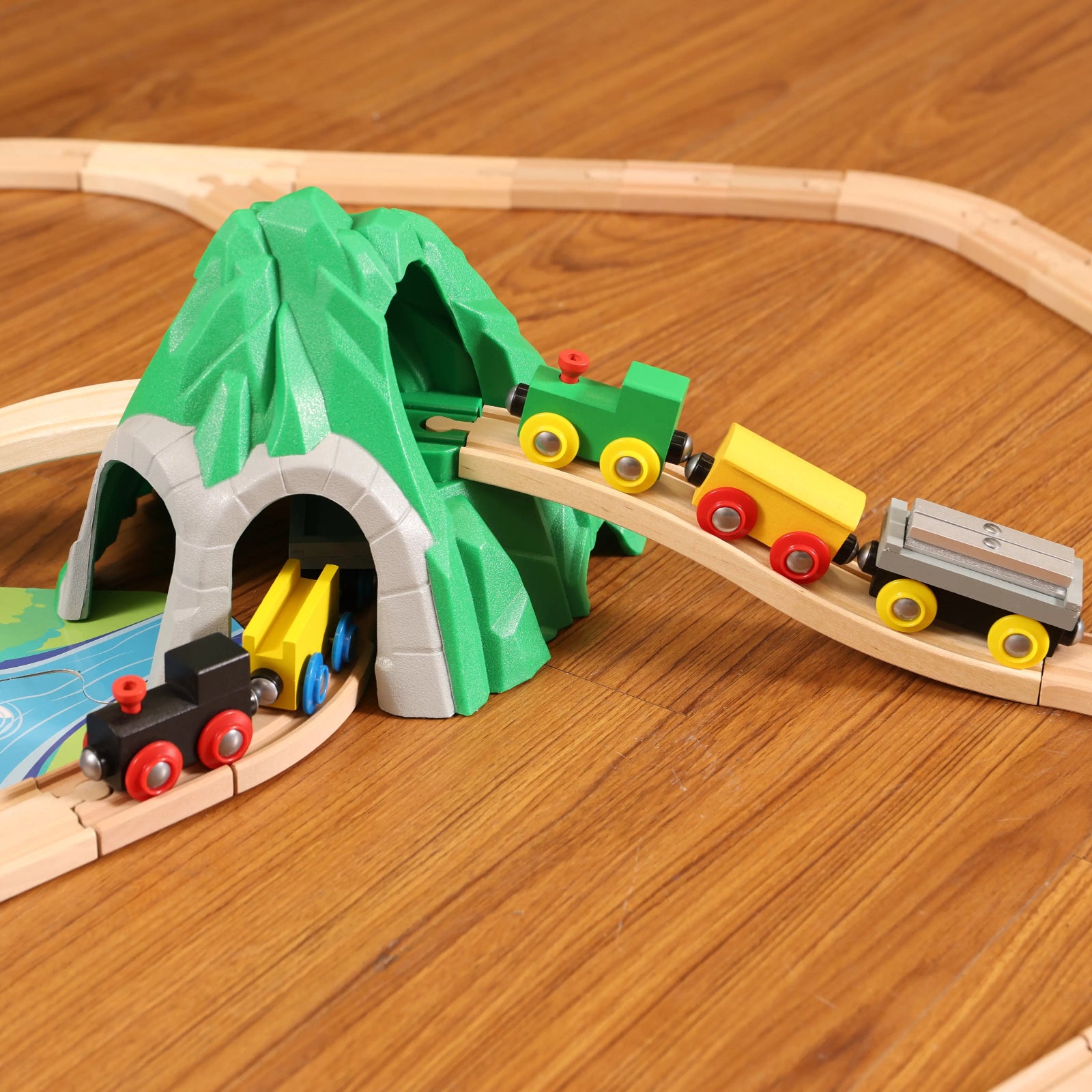 Wooden toy train set with tracks, tunnel, and small trains on a wooden surface